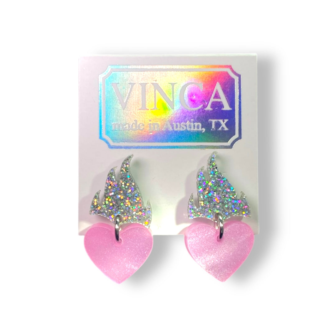 Flaming heart earrings in pearl pink and glitter hologram on a white card against a white background.