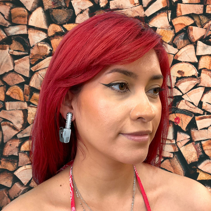 Chainsaw earring worn by a woman with bright red hair and alternatively styled.