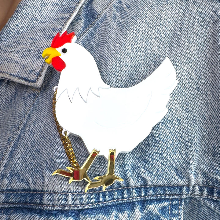 A farm animal chicken is pinned next to the lapel of a blue jean jacket.