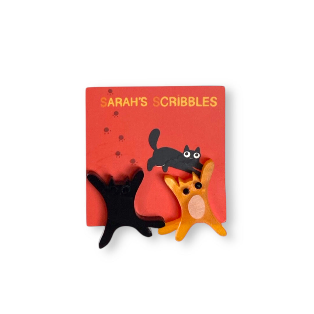 Two asymmetrical cat earrings on a Sarah's Scribbles' branded red card.