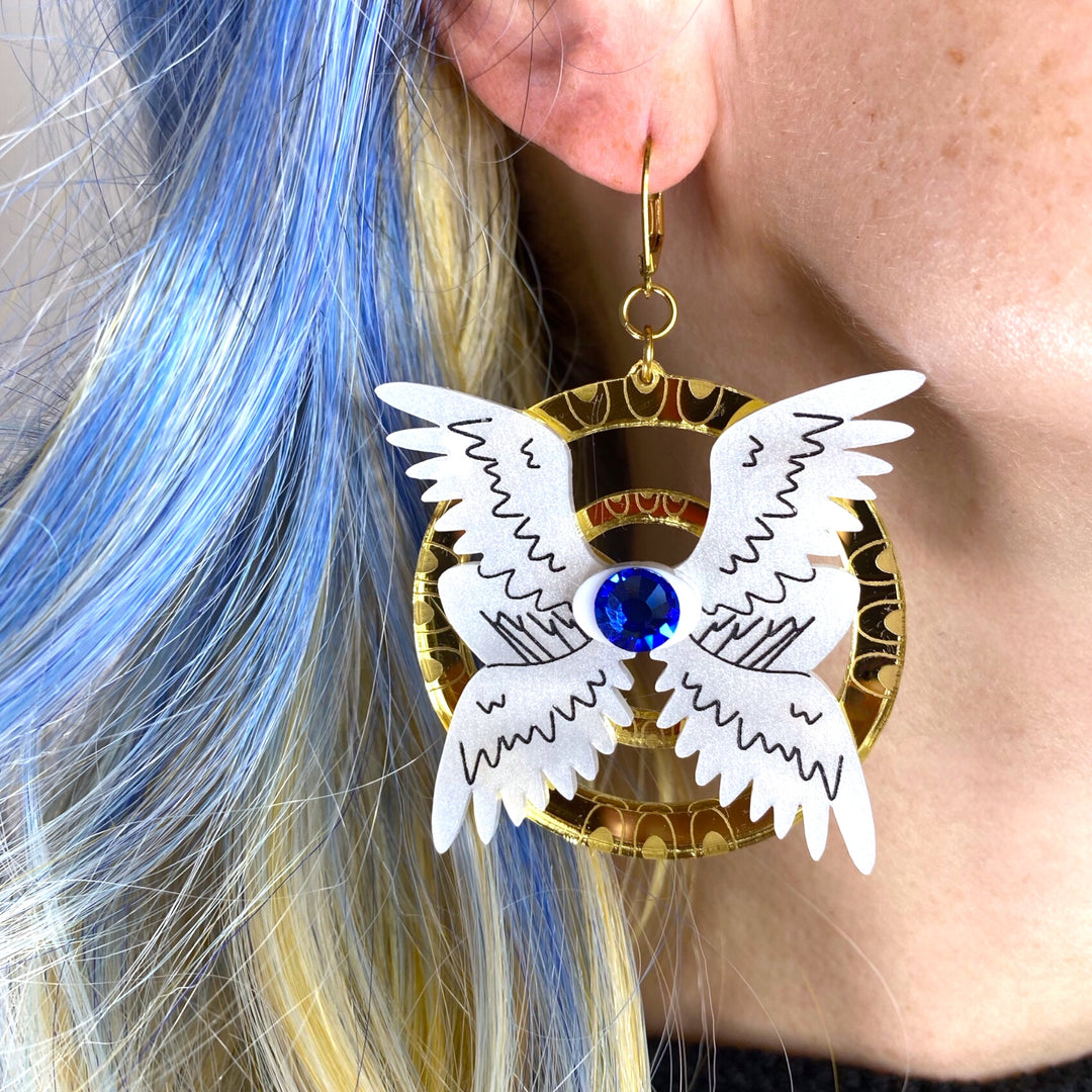 A woman with bright blue hair wears our handmade Sarah's Scribbles Seraphim angel dangle earrings.