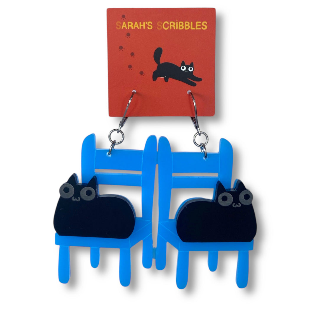 Our handmade Sarah's Scribbles black Cat on a Bright Blue Chair earrings float on a solid white background.