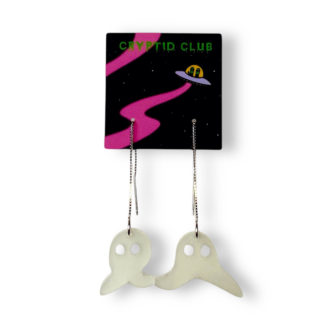 Our Sarah's Scribbles Cryptid Club ear threader earrings are threaded through a small Cryptid Club branded card and set against a white background.