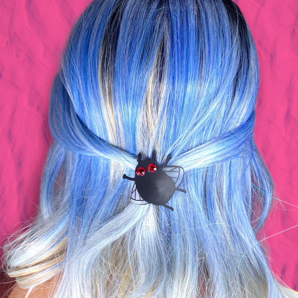 A woman with bright blue hair wears our Sarah's Scribbles Cryptid Club Moth Man hairclip.