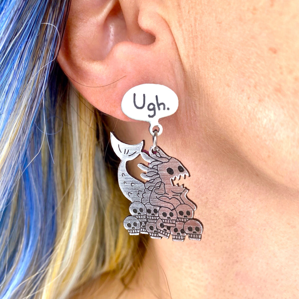 Sarah's Scribbles Cryptid Club Ugh. Mermaid Dangle Earrings on a model with bright blue hair.