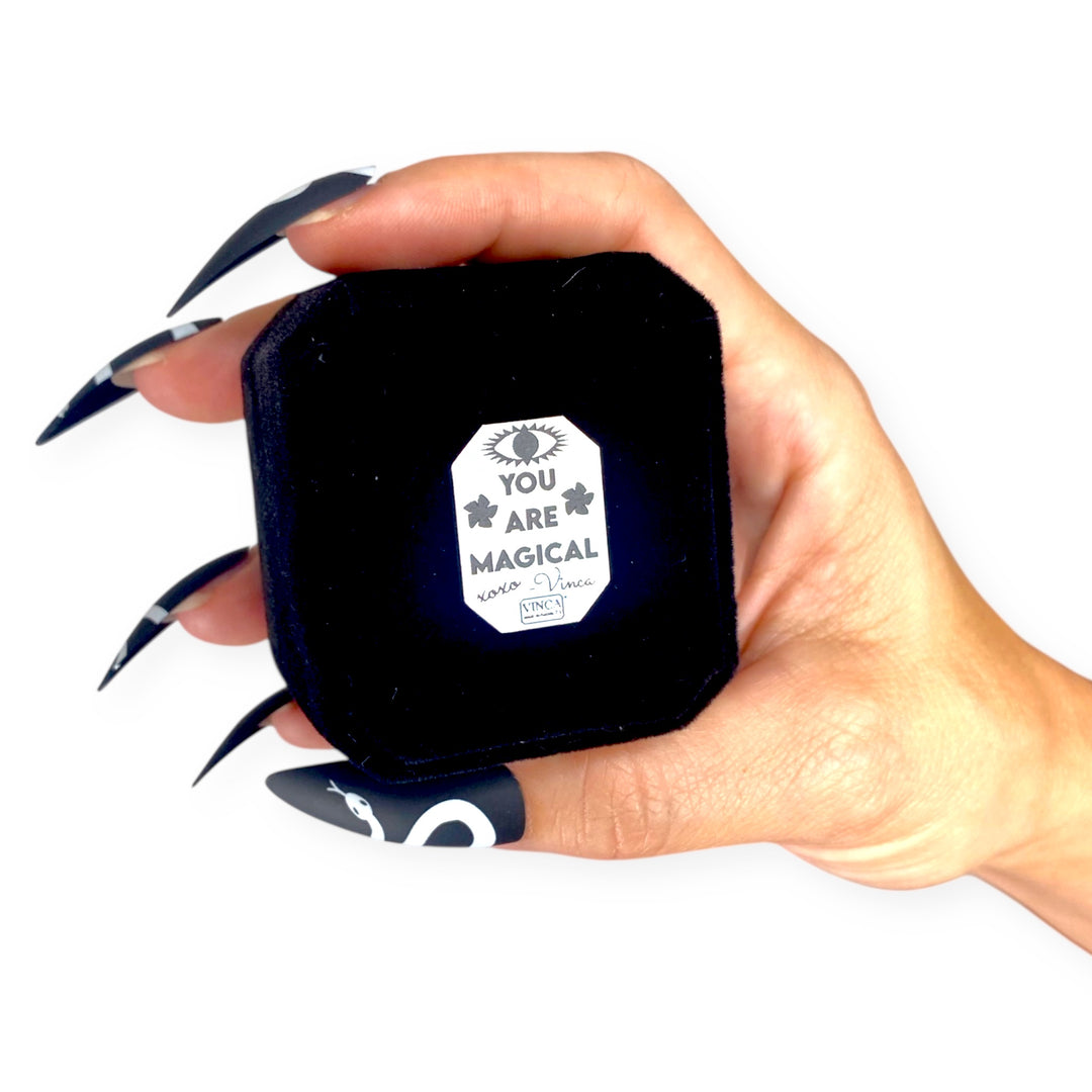 Hand holding a small black velvet ring box with a 'You Are Magical' label.