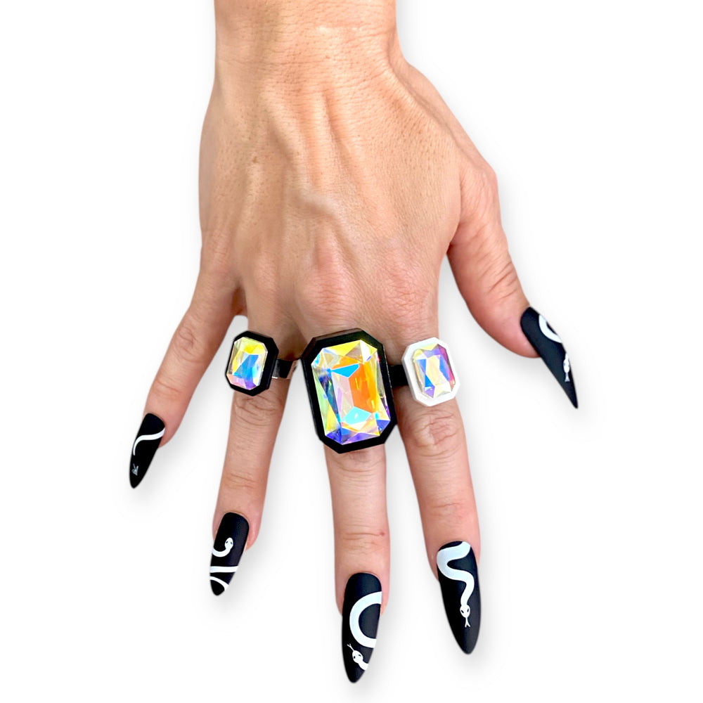 Hand wearing colorful gemstone rings with black and white nails.