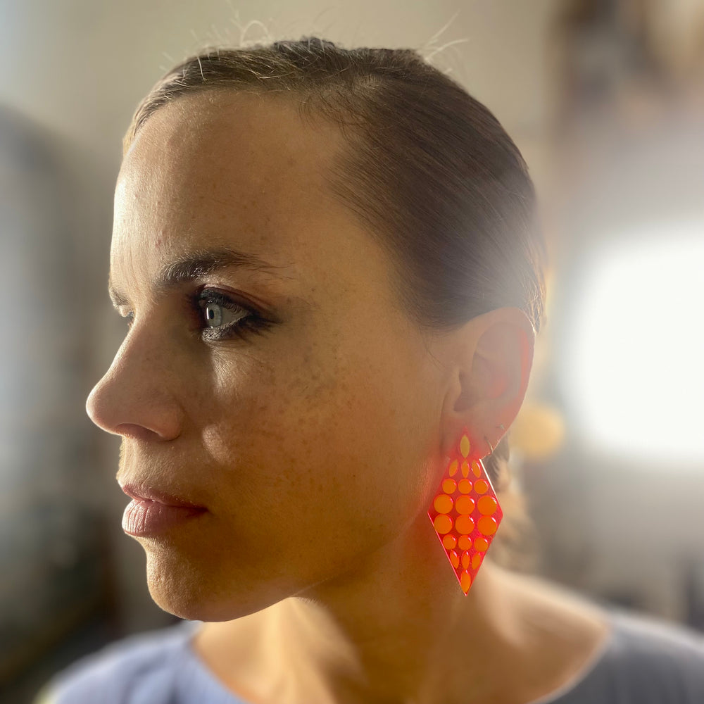 Close-up of a woman wearing transparent neon pink geometric earrings with a blurred background.