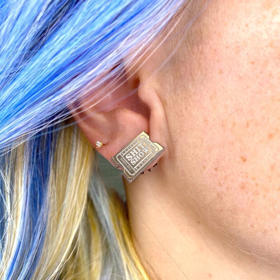 Antique golden ticket Earring with 'SHIT SHOW' text worn by a person with colorful hair.