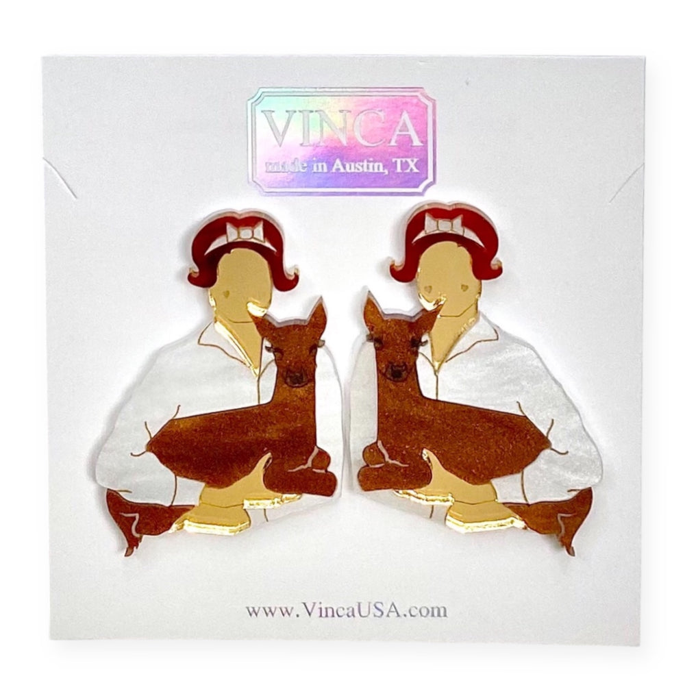 A pair of Audrey Hepburn-inspired statement earrings with a woman holding a deer on a white Vinca branded card.