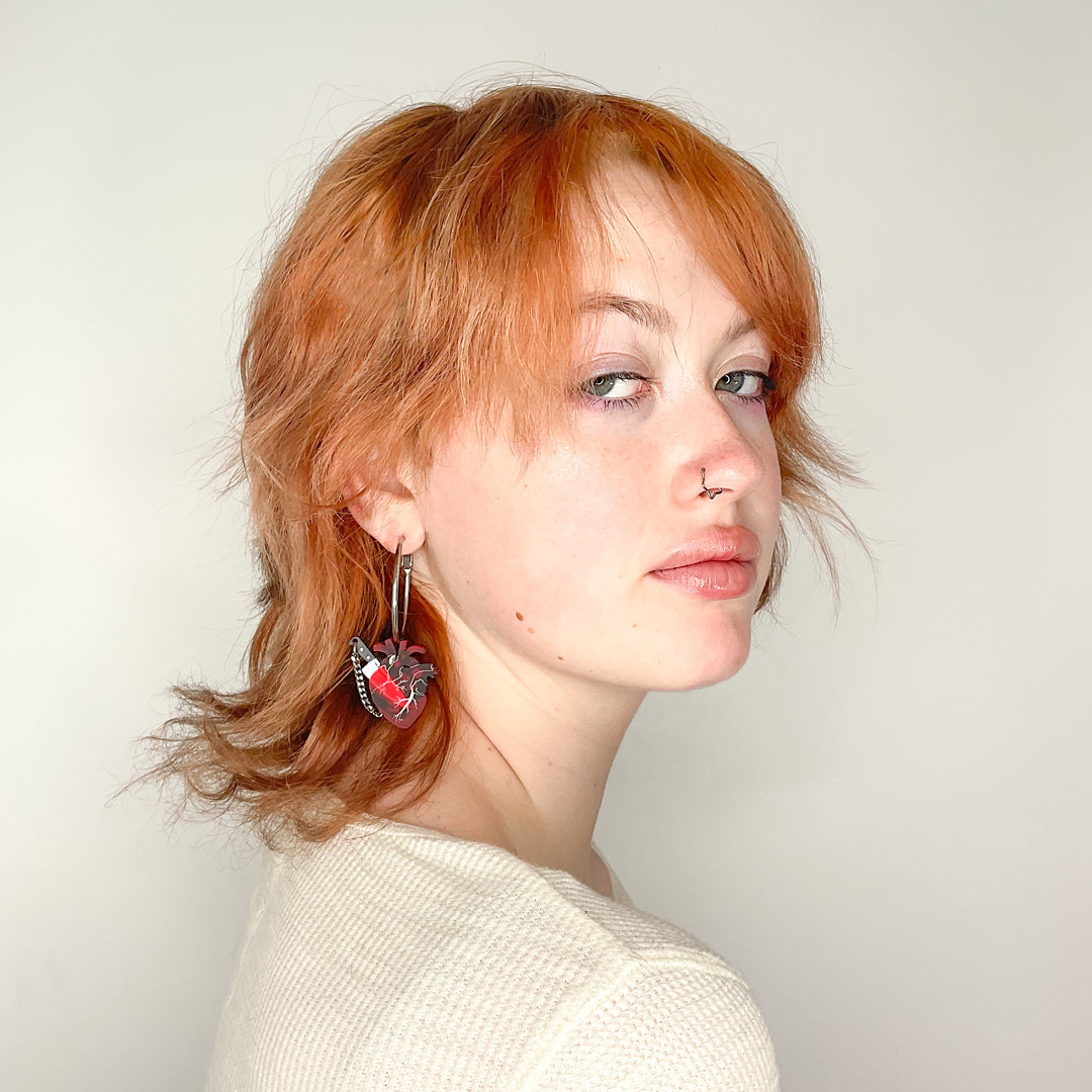 Chopped heart hoops on a model for scale. Stainless steel hoops with transparent, frosted red anatomical hearts with plastic knife charms.