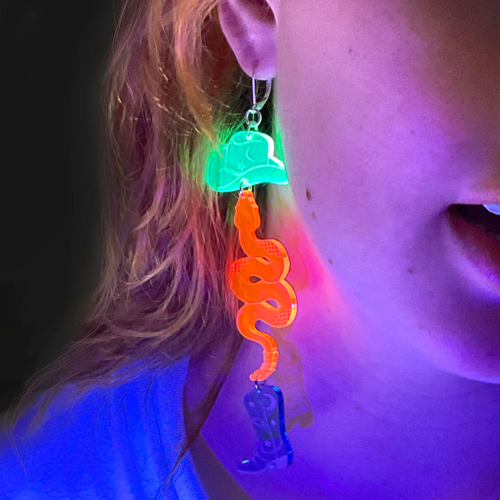 Our Neon Cowboy earrings are worn by a young woman and glow under a black light. 