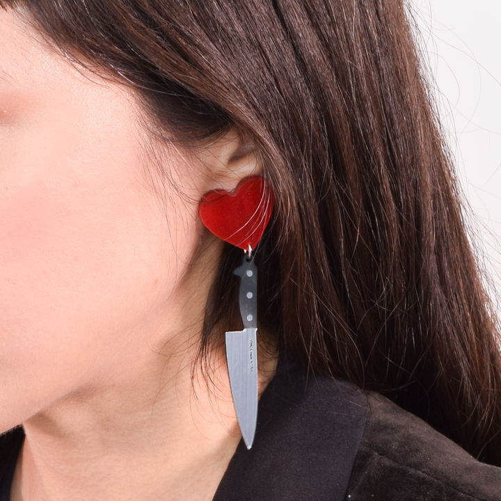 I heart knife earrings on an ear of a woman with brown hair. 