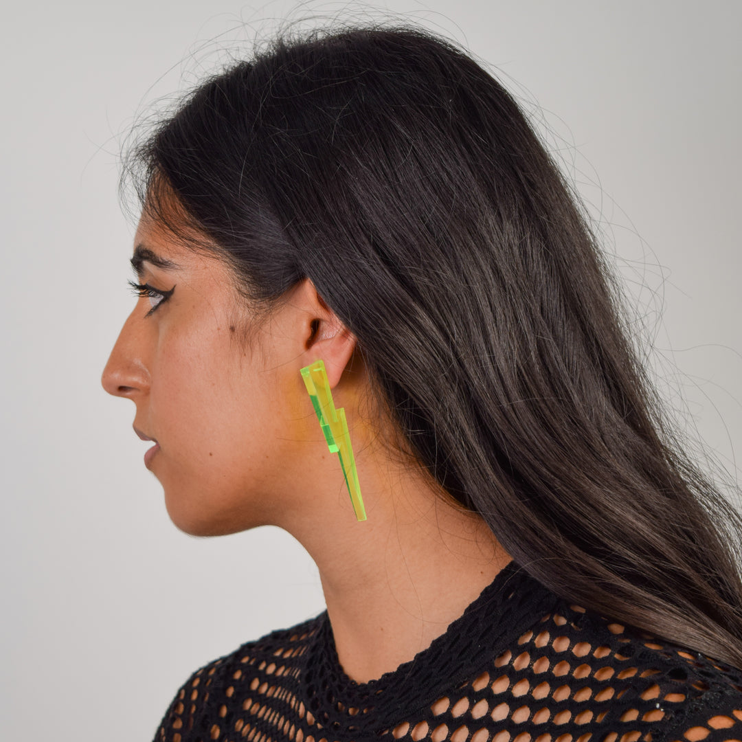 A model with long black hair wears a transparent neon green lightning bolt earring.